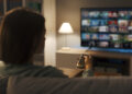 Young woman relaxing on the couch at home and watching videos on demand on her TV, entertainment concept